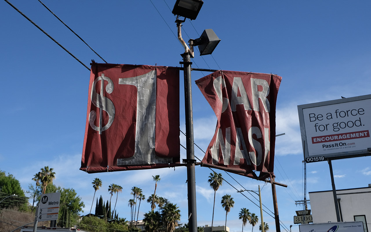 Digital Photo - Red degenerating one dollar car wash sign with white text with an  advertising billboard, palm trees, and blue Los Angeles sky in the background.
