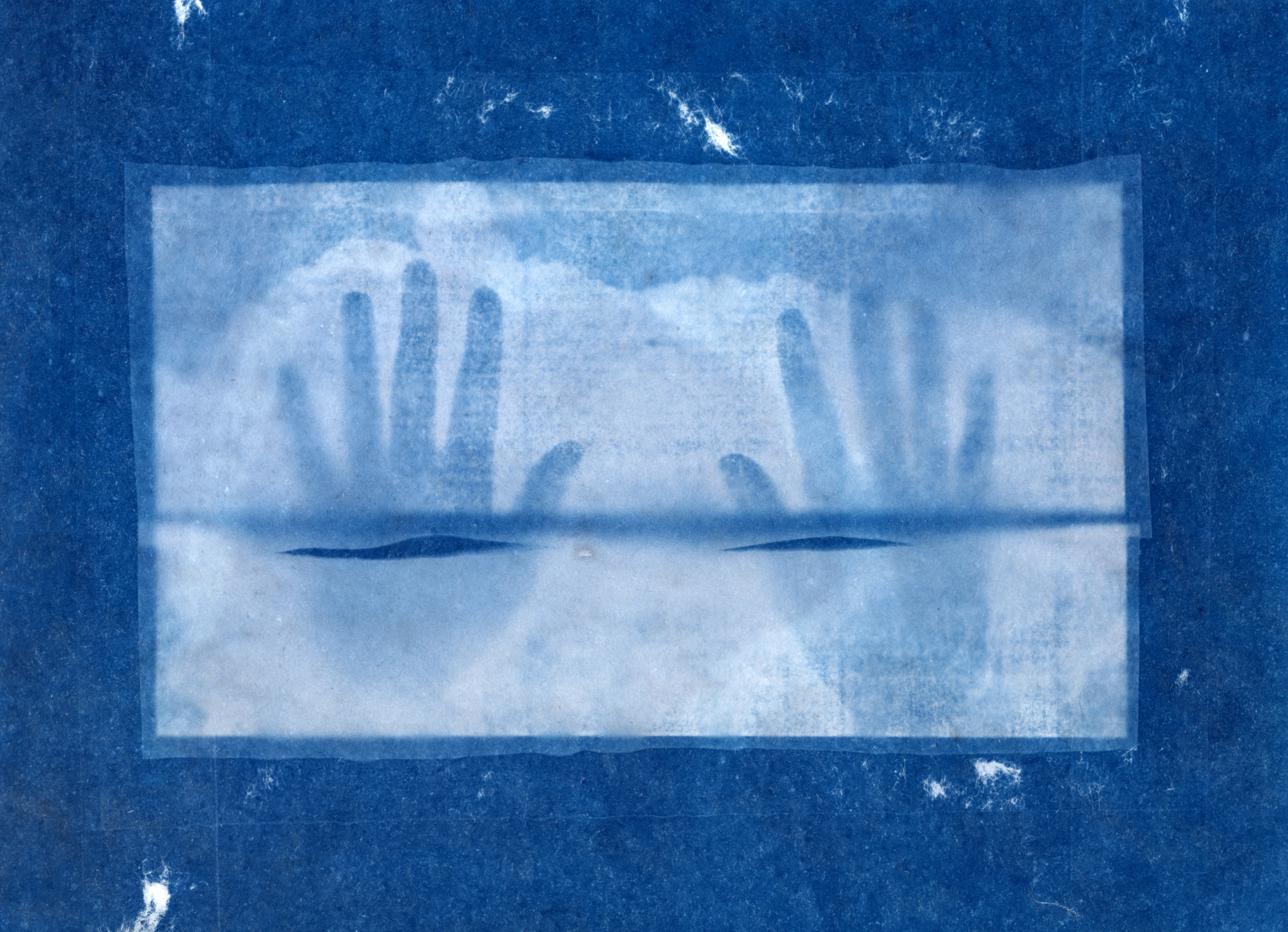 A cyanotype of two hands that appear silhouetted. The hands and background are
darker blue and the frame they sit in are lighter blue.